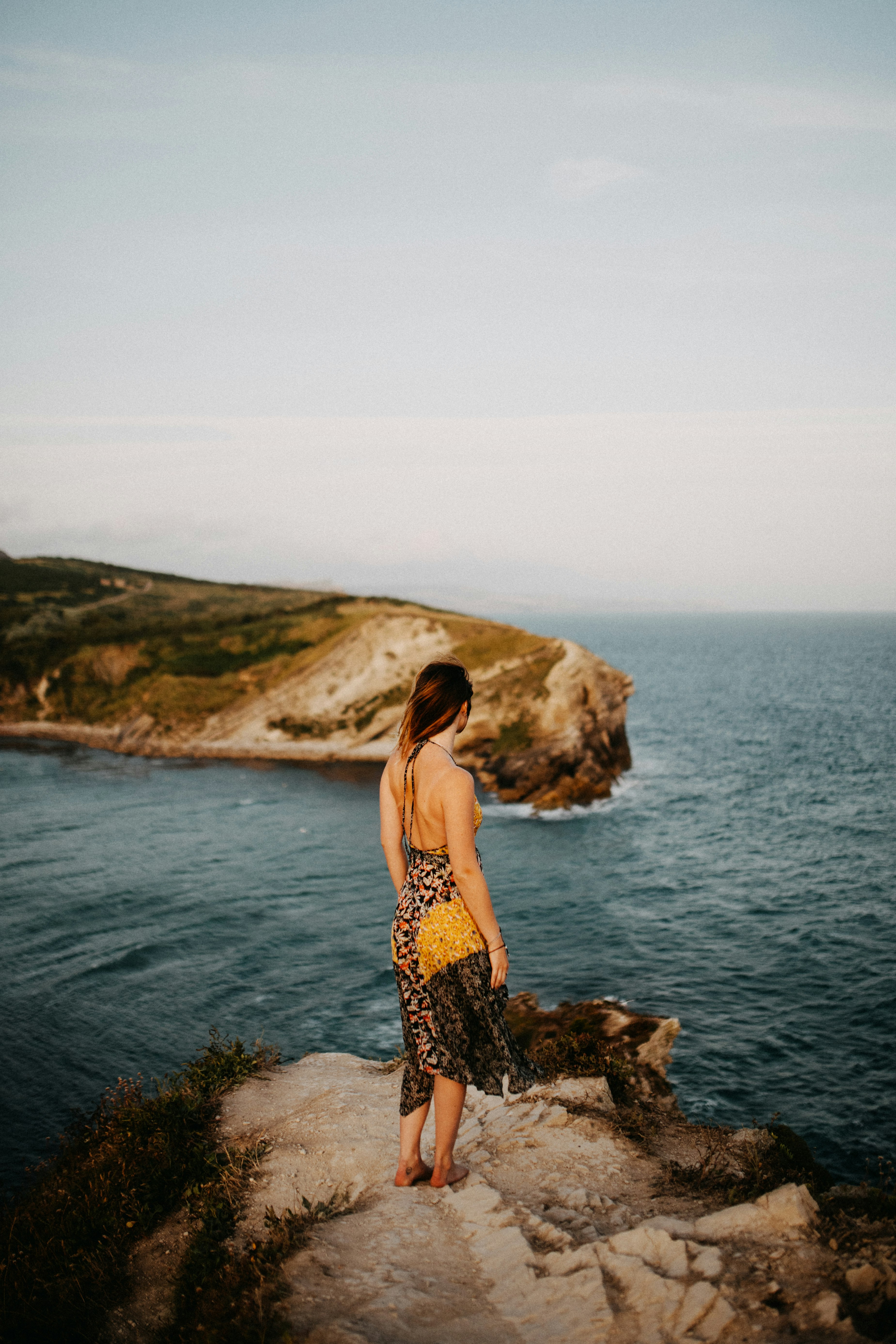 woman in black and brown floral dress standing on rock formation near body of water during